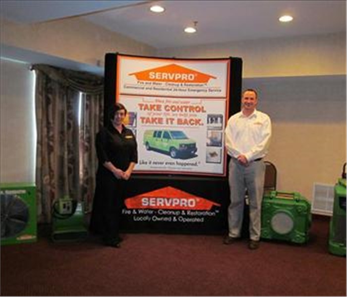 A male and female employee standing next to a large SERVPRO banner